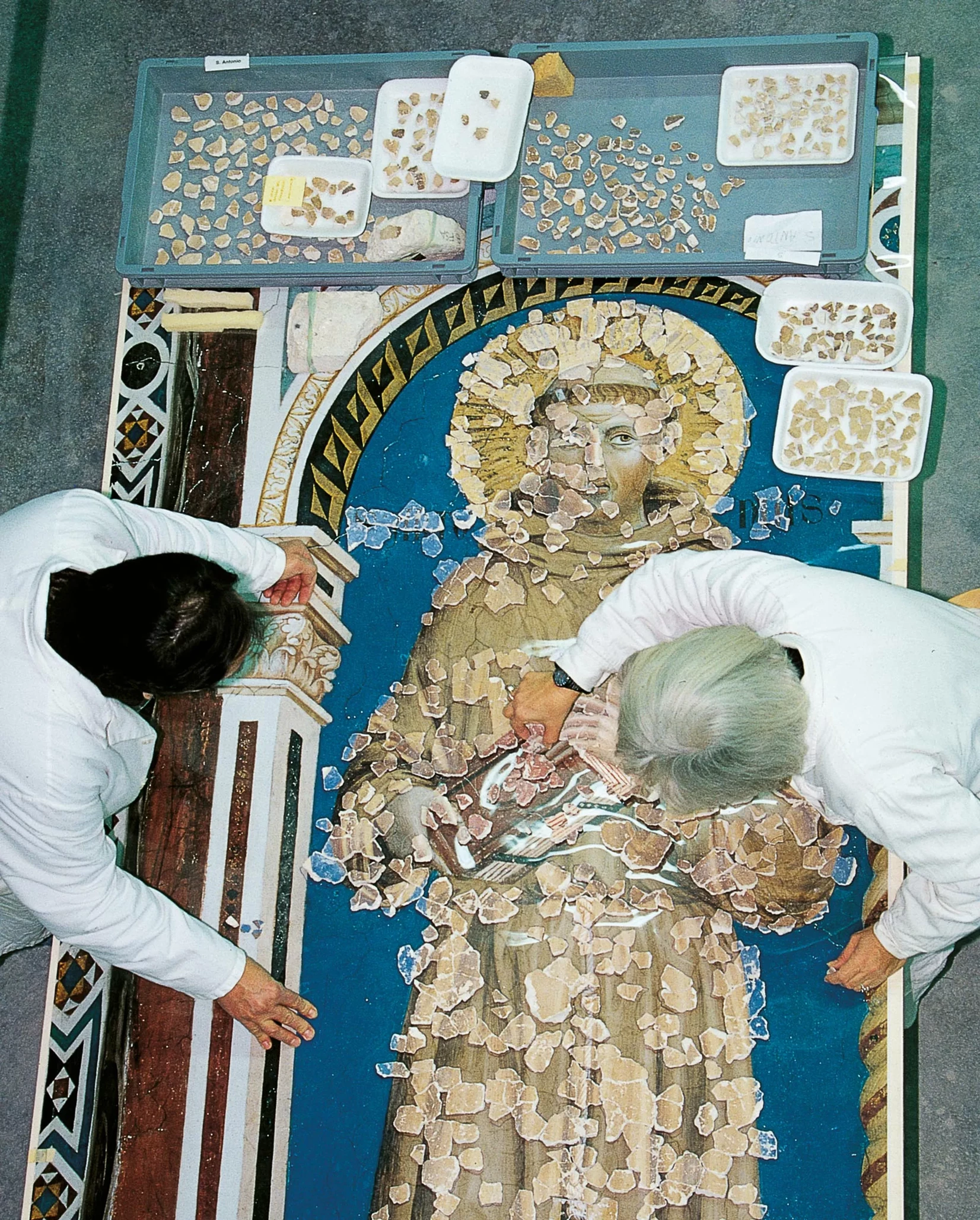Restorers reassemble small painted fragments around the figure of a saint.