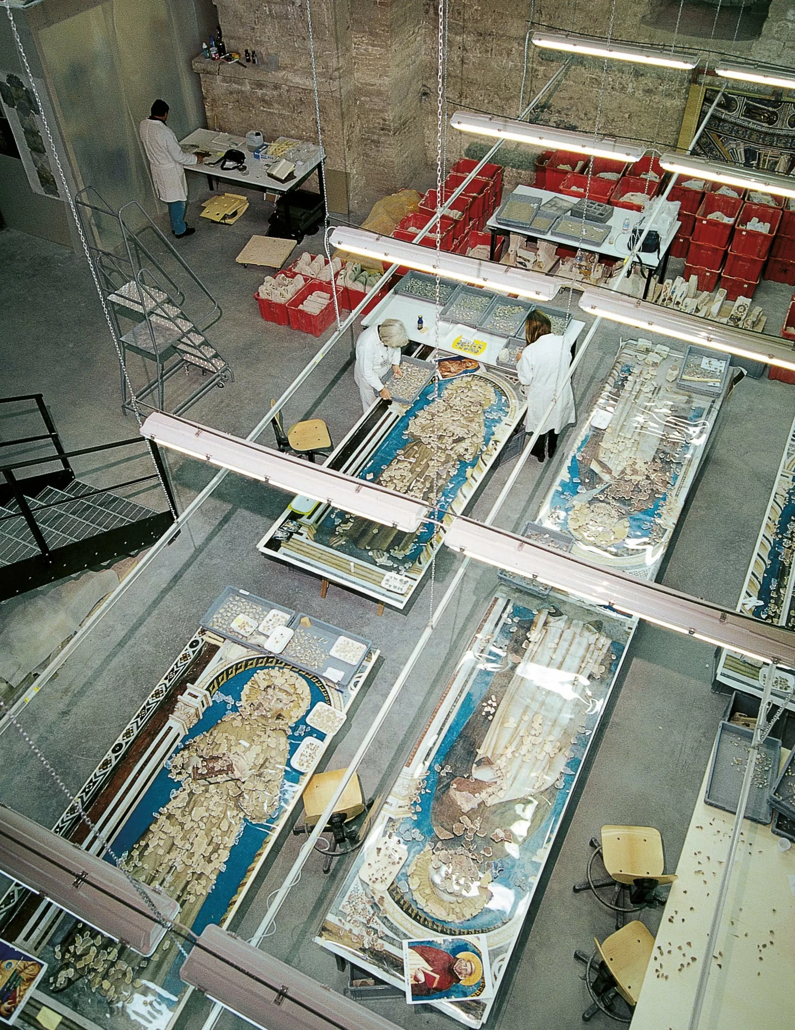 Restoration workshop seen from above: painted fragments sorted and reassembled on large tables.