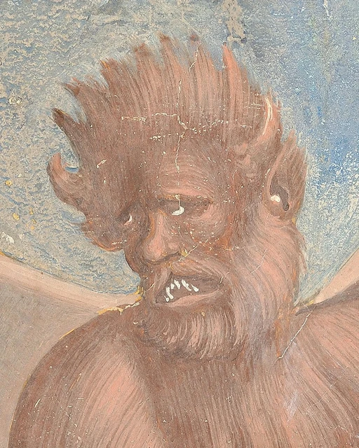 Frontal view of a reddish demon with horns, a beard and protruding teeth.